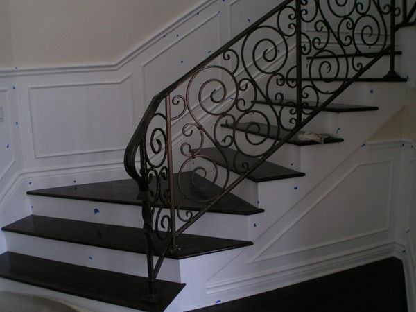 Elegant curved staircase with black steps and ornate wrought-iron railing in a white interior.