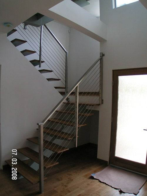 Indoor staircase with metal railing and wooden steps in a bright entryway, beside a glass door.