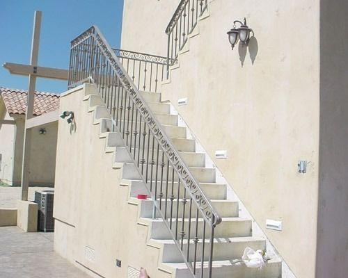 Outdoor concrete stairs with metal railings beside a beige stucco building