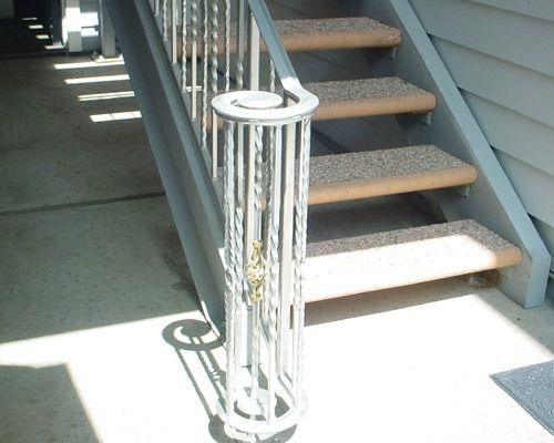 White cylindrical bike rack beside an outdoor staircase in bright sunlight