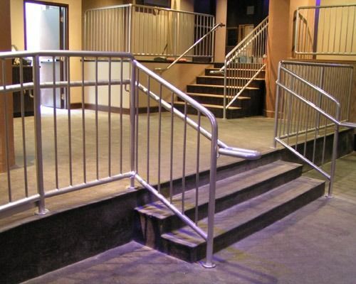 Metal railings and ramps leading to steps in a dimly lit indoor entrance area
