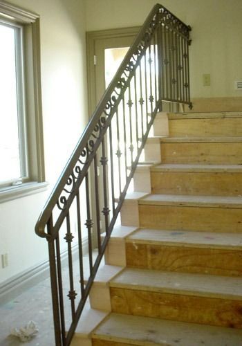 Indoor staircase with light wood steps and a dark metal handrail beside a window