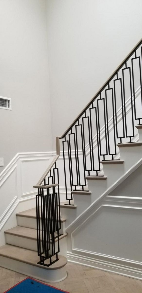 Staircase with black wrought-iron railing and white wainscoting in a bright interior hallway