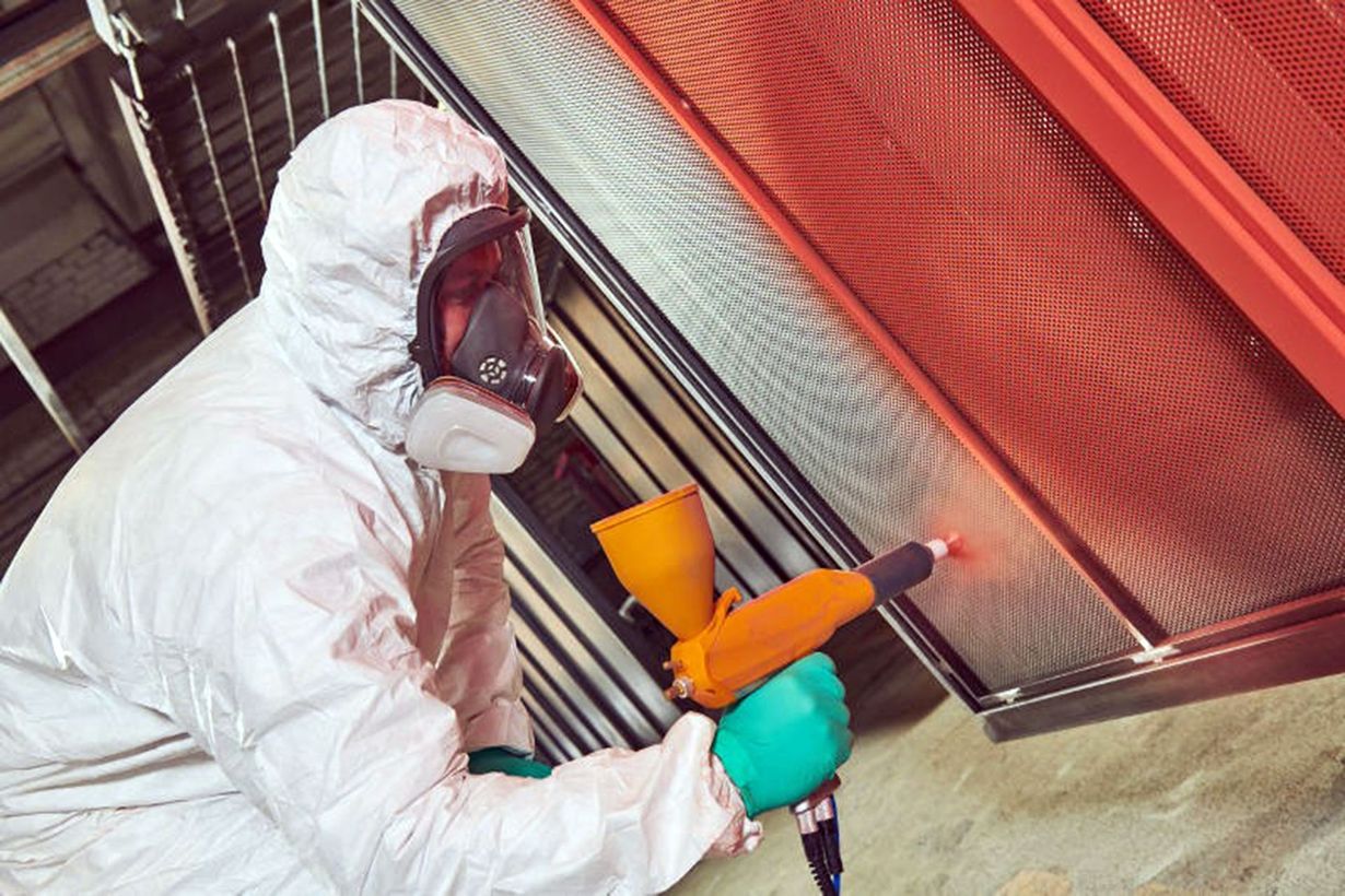 Worker in white protective suit spray-painting a red metal gate with an orange sprayer