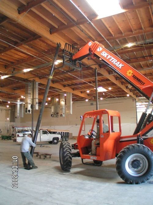 Orange SKYTRAK forklift lifting materials in a warehouse, with worker below and white pickup nearby