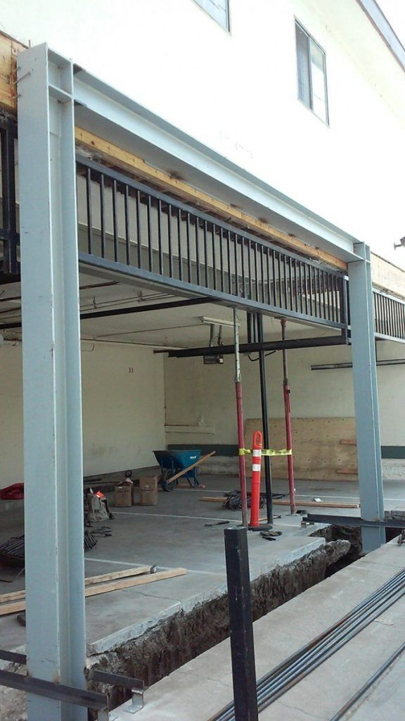 Raised metal canopy under construction beside a building, with scaffolding and exposed beams.
