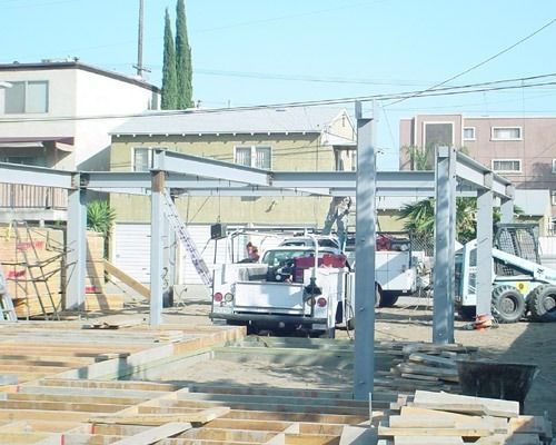 Construction site with steel frame, white trucks, and buildings in the background