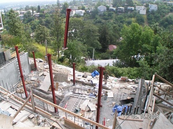 Construction site with red steel beams overlooking a green hillside and distant buildings
