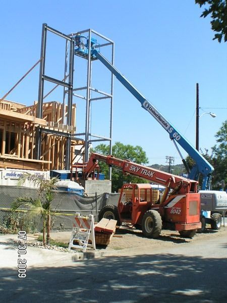 Construction site with two boom lifts working beside a partially built wooden structure