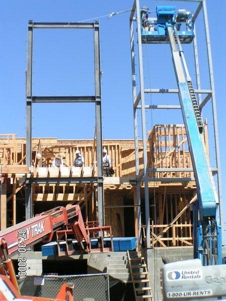 Construction site with wooden framing, a blue lift, and workers on scaffolding under a clear sky