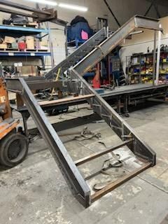 Large metal staircase assembly in a workshop, with black ramps and silver supports on a concrete floor.