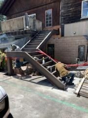 Worker repairing a damaged outdoor staircase beside a brick building and deck