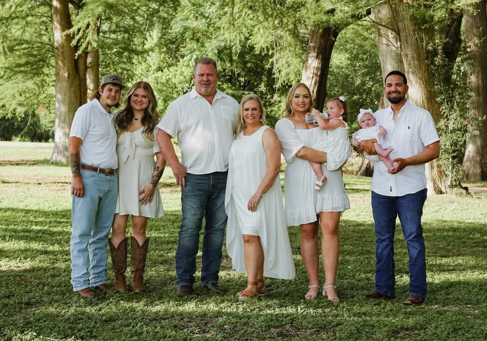 Family group posing outdoors; six adults, two babies, all dressed in white and denim.