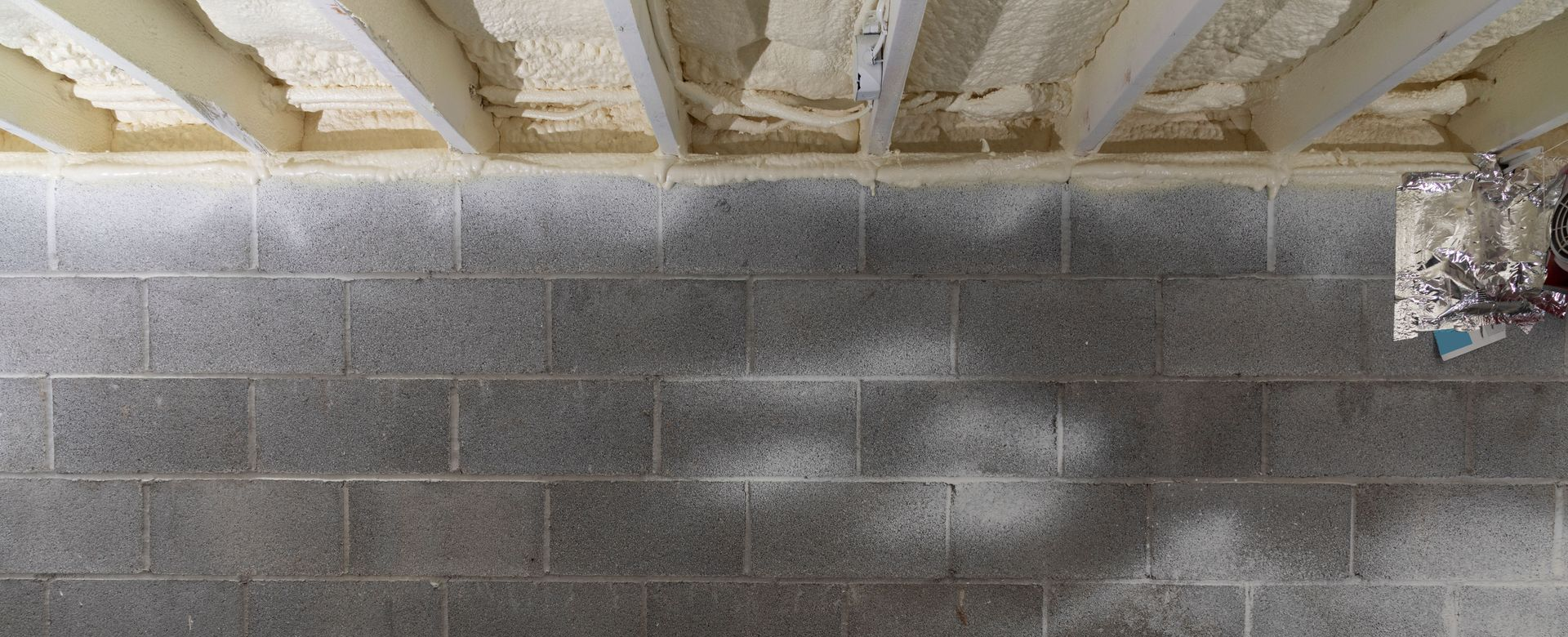 Basement wall with spray foam insulation under the ceiling. Concrete block wall with areas of discoloration.