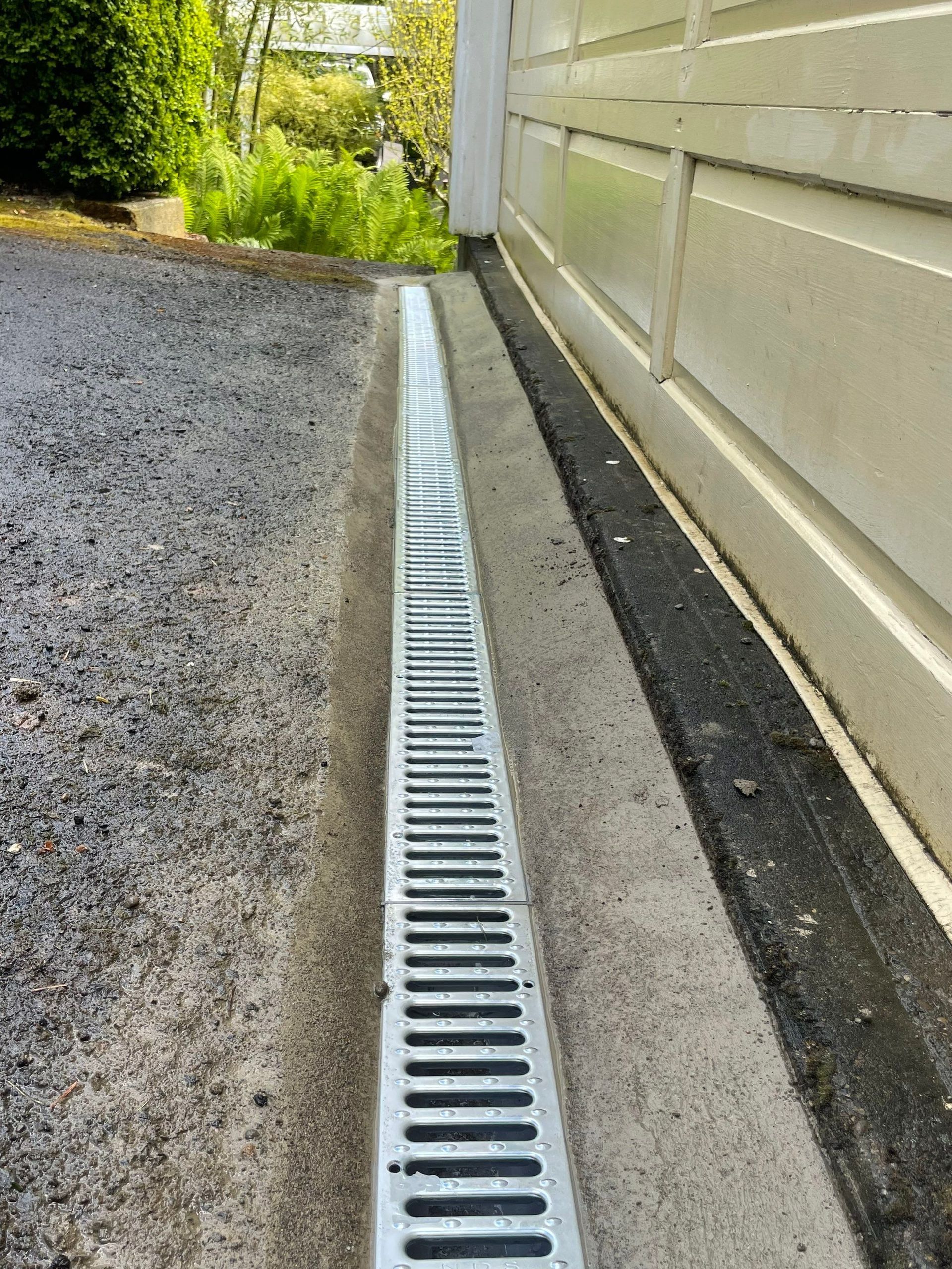 A French drain is installed on the side of a garage door.