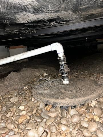 A sump pump is installed beneath a layer of rocks in the basement.