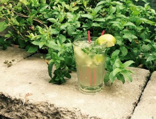 A glass of lemonade with a straw in it is sitting on a stone ledge.