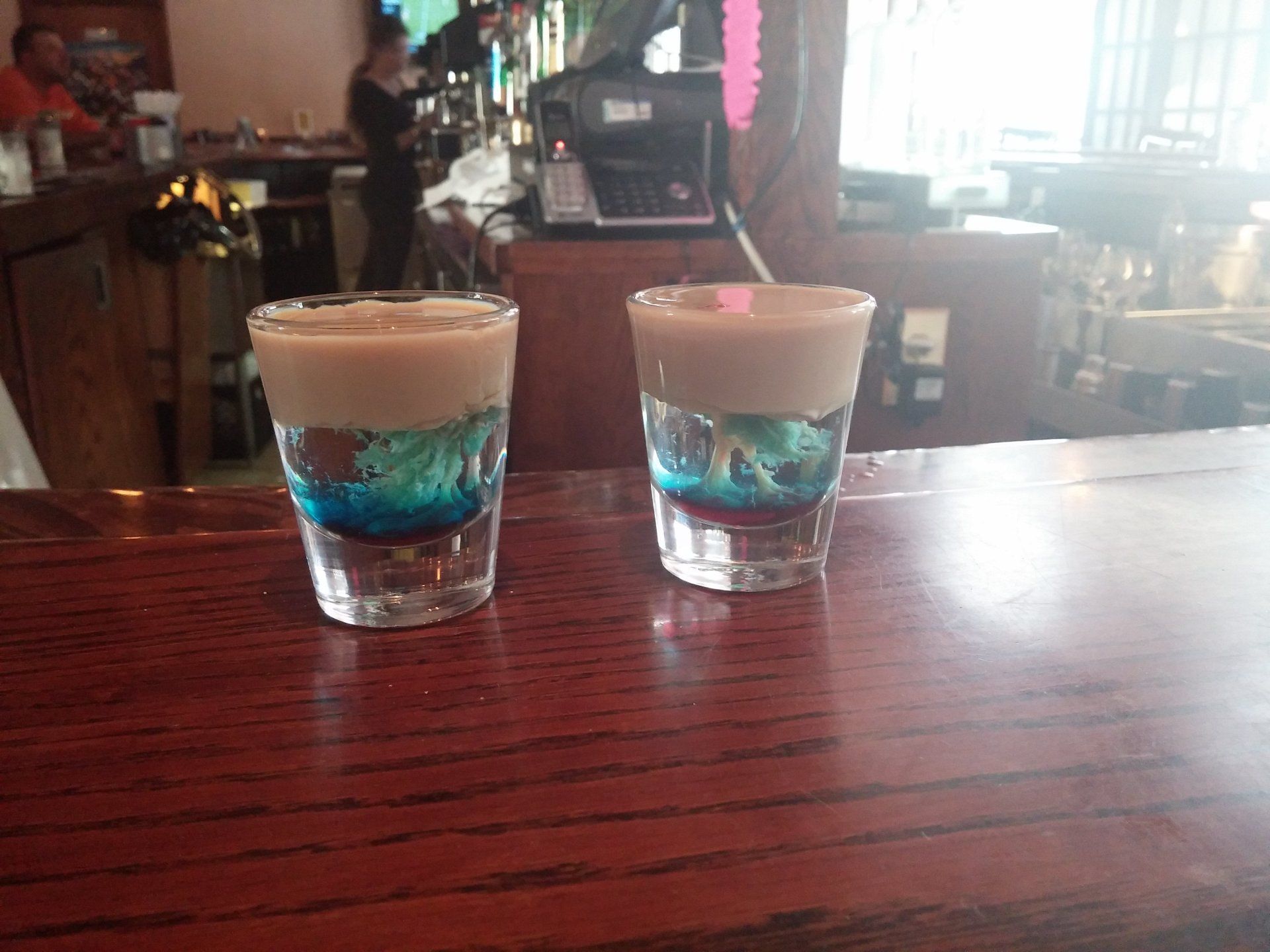 Two shot glasses are sitting on a wooden bar top