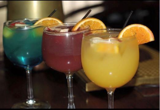 Three different colored drinks in wine glasses on a table