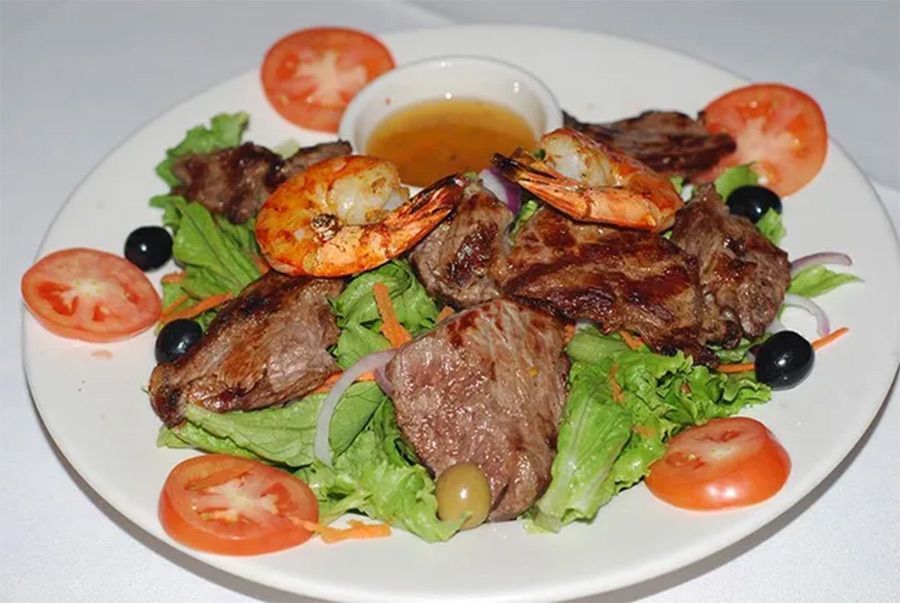 A white plate topped with meat, shrimp, tomatoes and olives