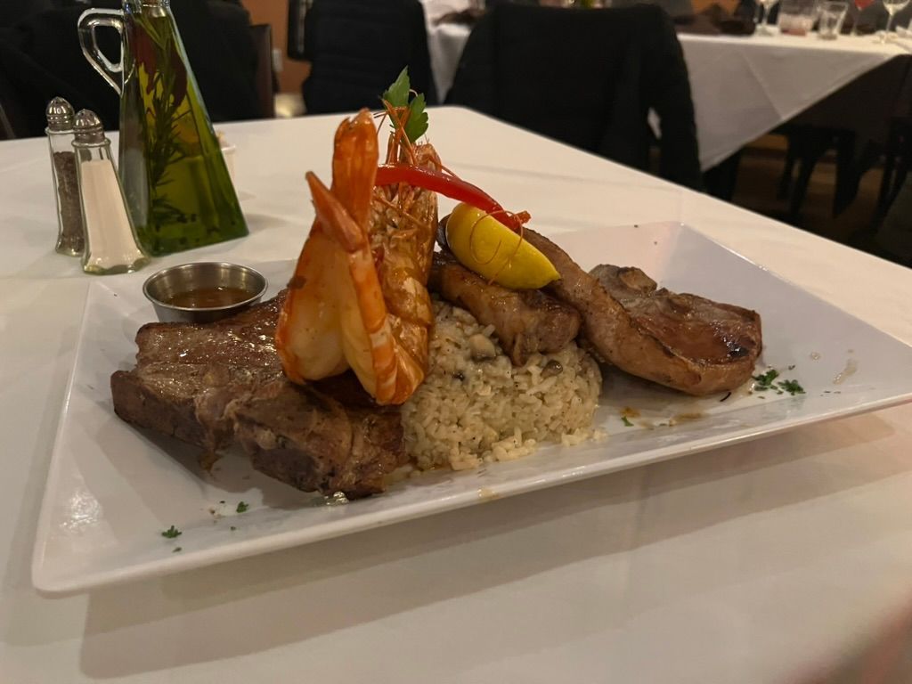 A white plate topped with meat, shrimp, and rice on a table.