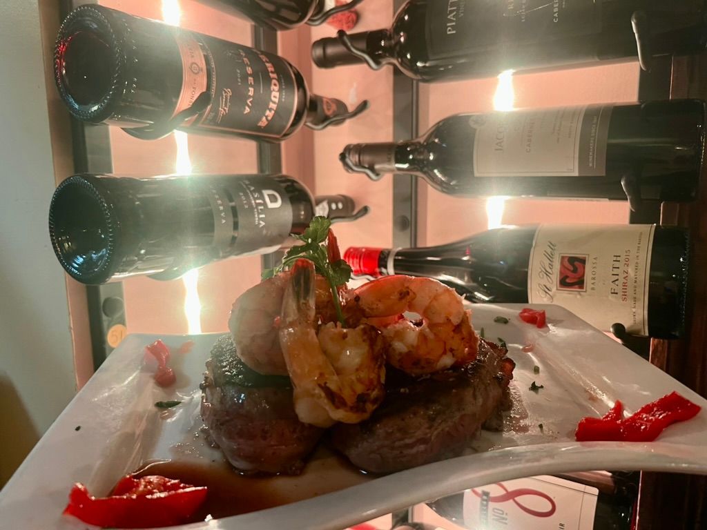 A plate of food with shrimp and a bottle of wine in the background.