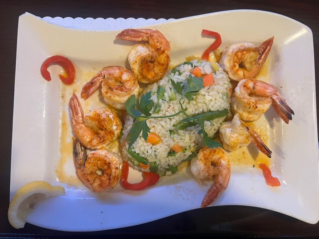 A white plate topped with shrimp and rice on a table.
