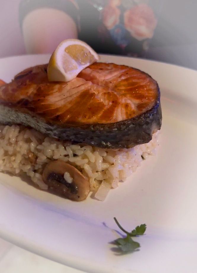 A white plate topped with a piece of salmon and rice