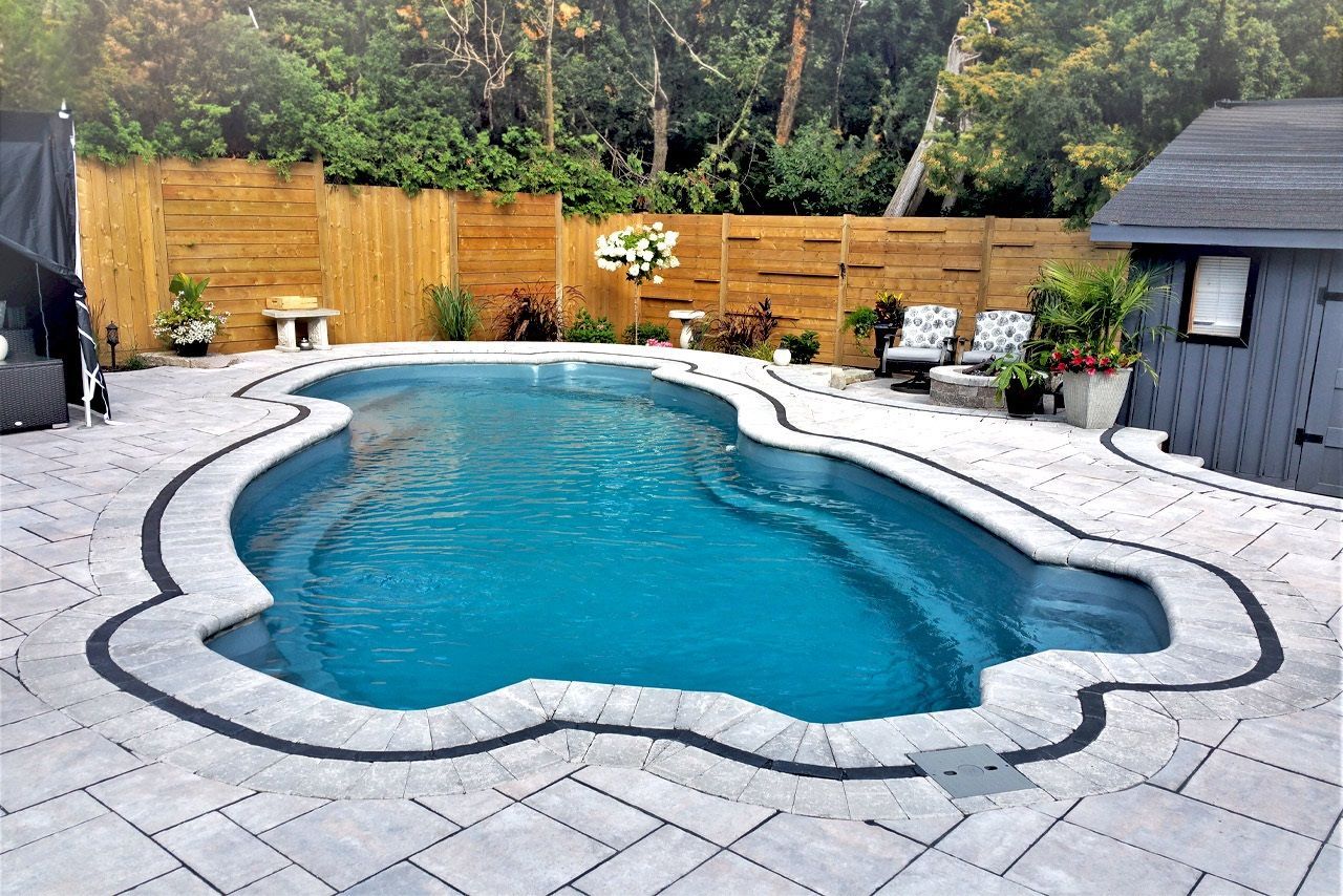 A large swimming pool is surrounded by a stone patio and a wooden fence.