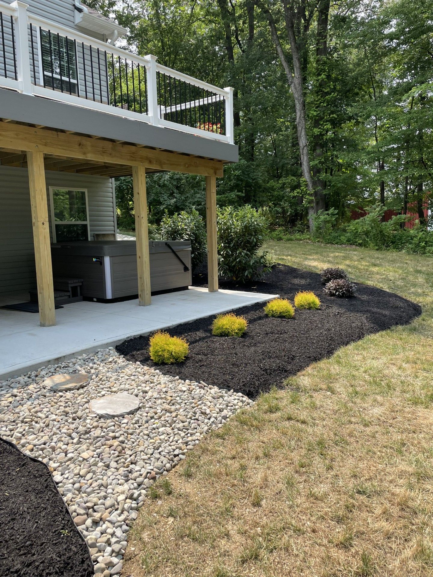 There is a deck with a hot tub underneath it in the backyard.