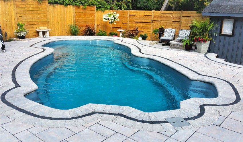 A large swimming pool is surrounded by a patio and a wooden fence.