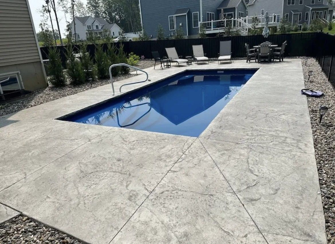 A large swimming pool with a concrete patio and chairs around it.