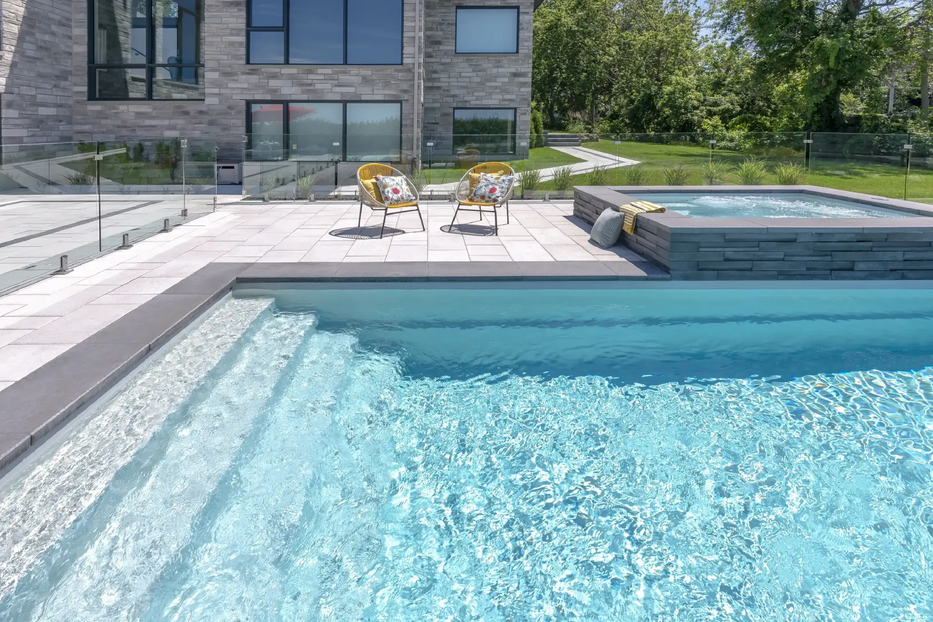A large swimming pool with chairs and a hot tub in front of a house.