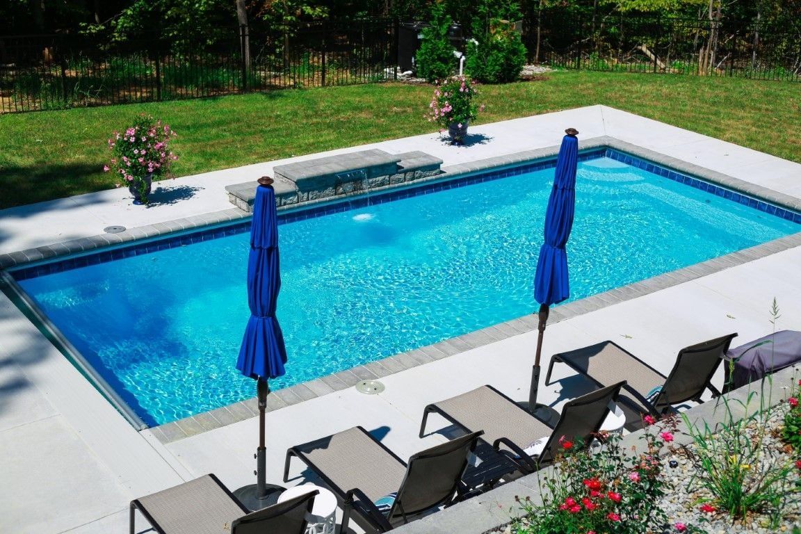 A large swimming pool surrounded by chairs and umbrellas in a backyard.