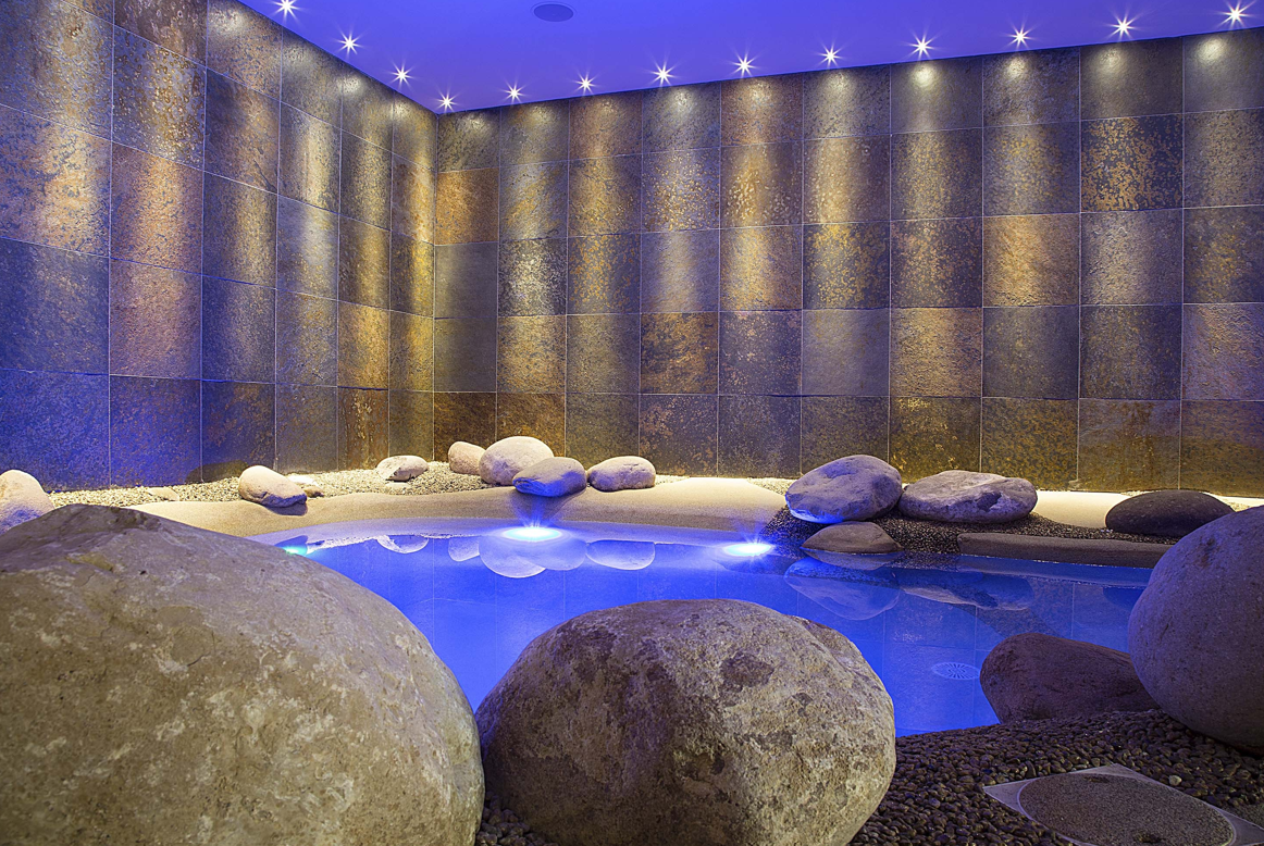 A large swimming pool surrounded by rocks in a room with blue lights.