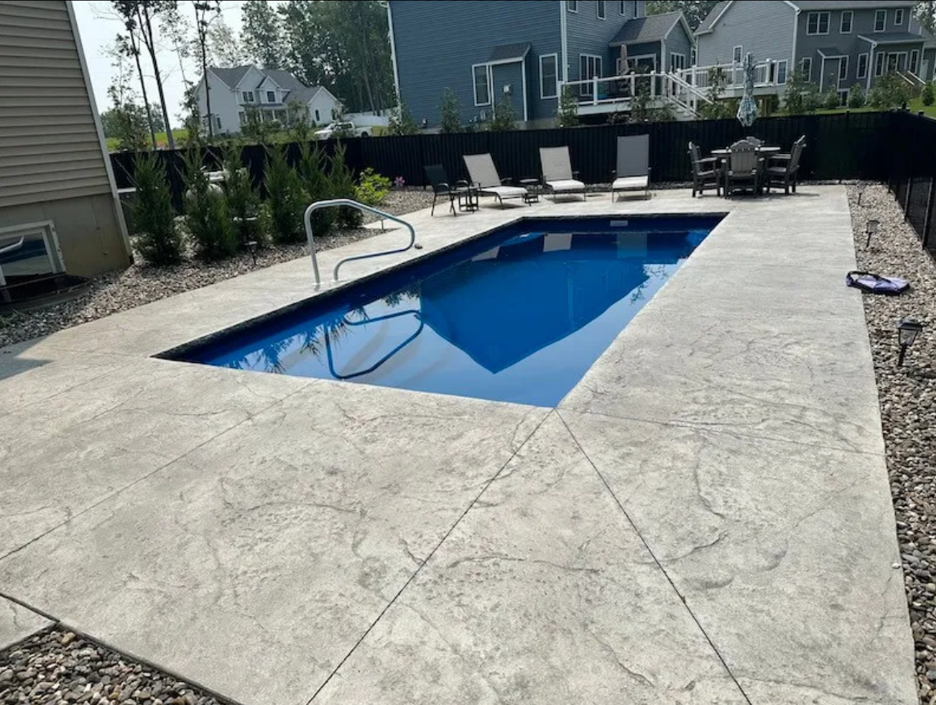 A large swimming pool is surrounded by chairs and a table.