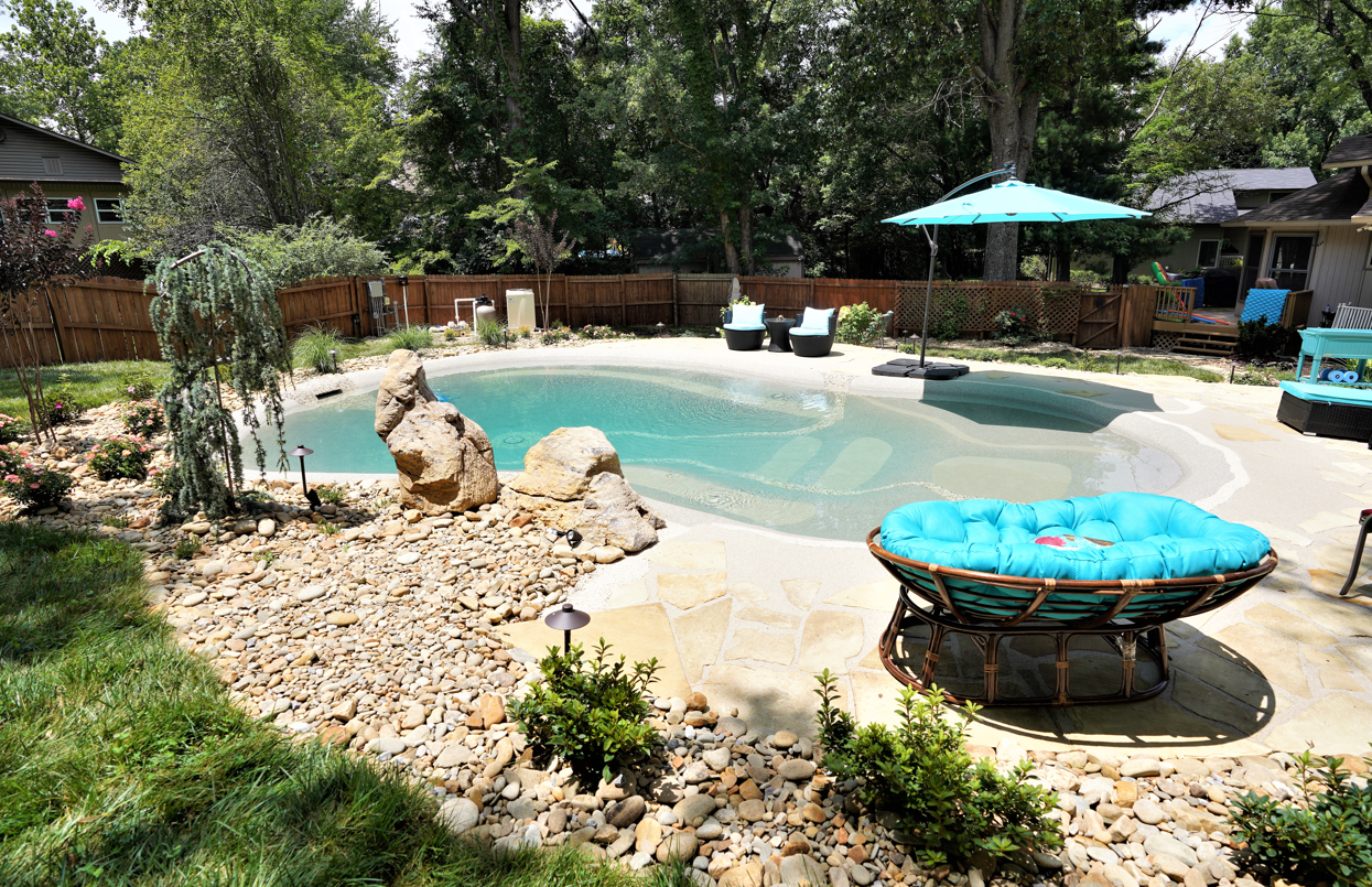 A large swimming pool in the backyard of a house with chairs and umbrellas.