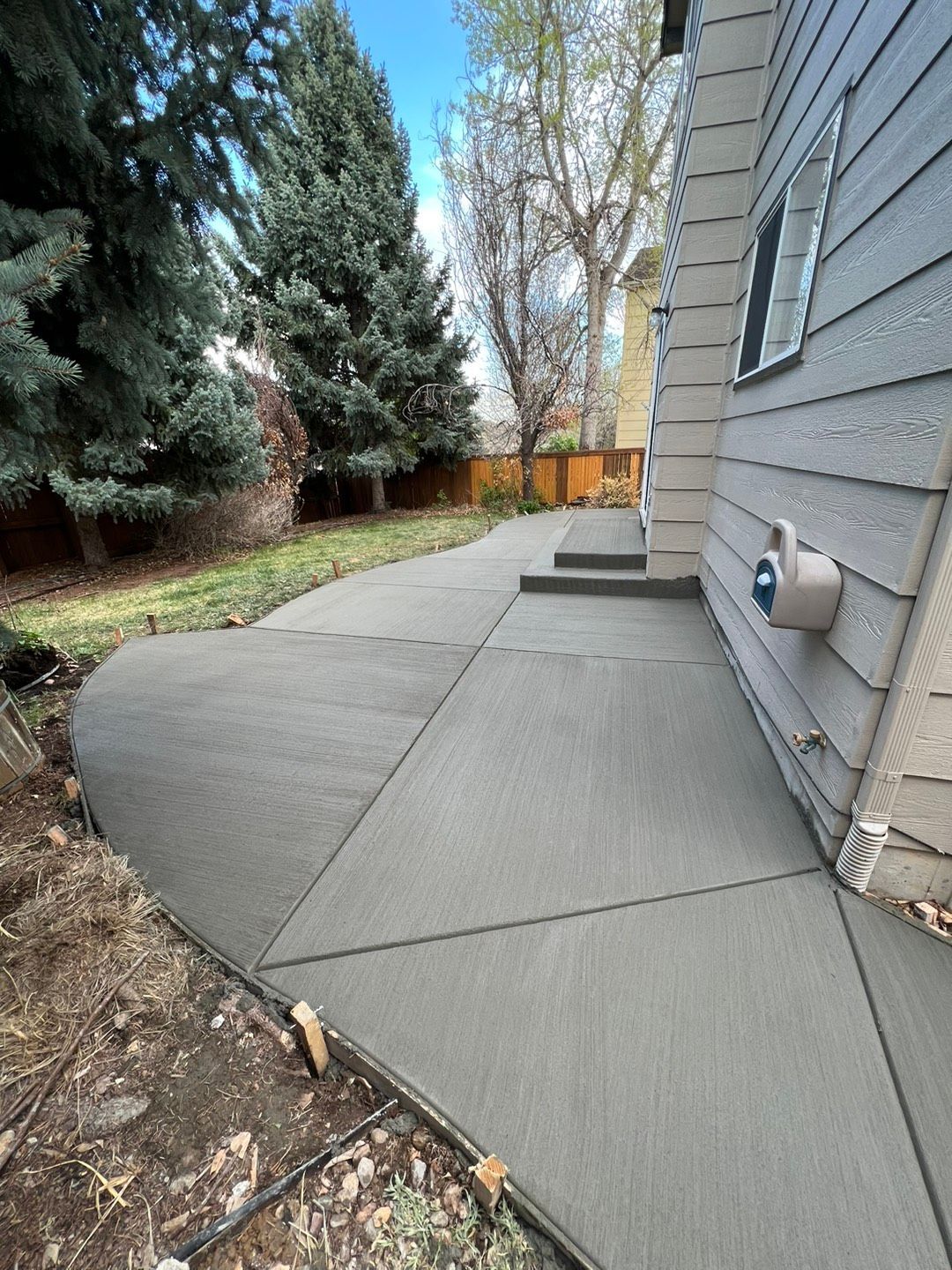 A concrete walkway leading to a house with trees in the background.