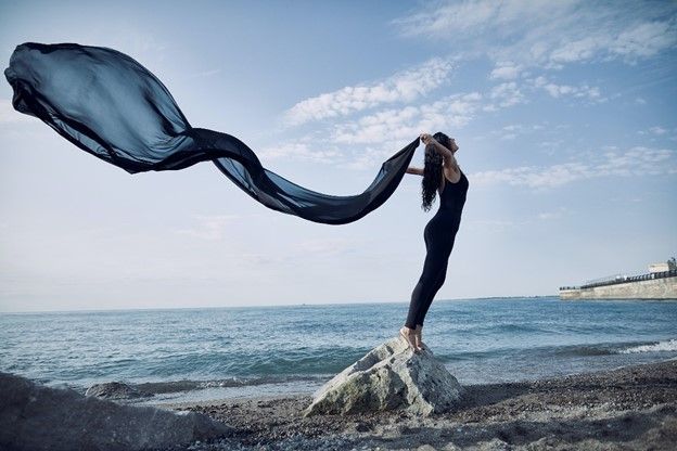 a woman is standing on a rock on the beach holding a long black cloth