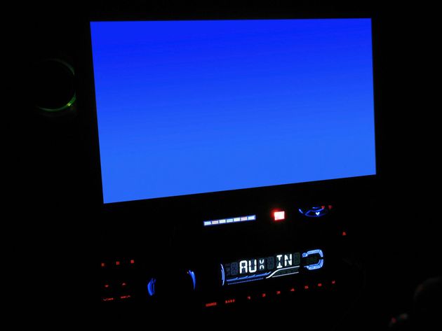 Car dashboard at night with a bright blue screen and illuminated stereo controls below.