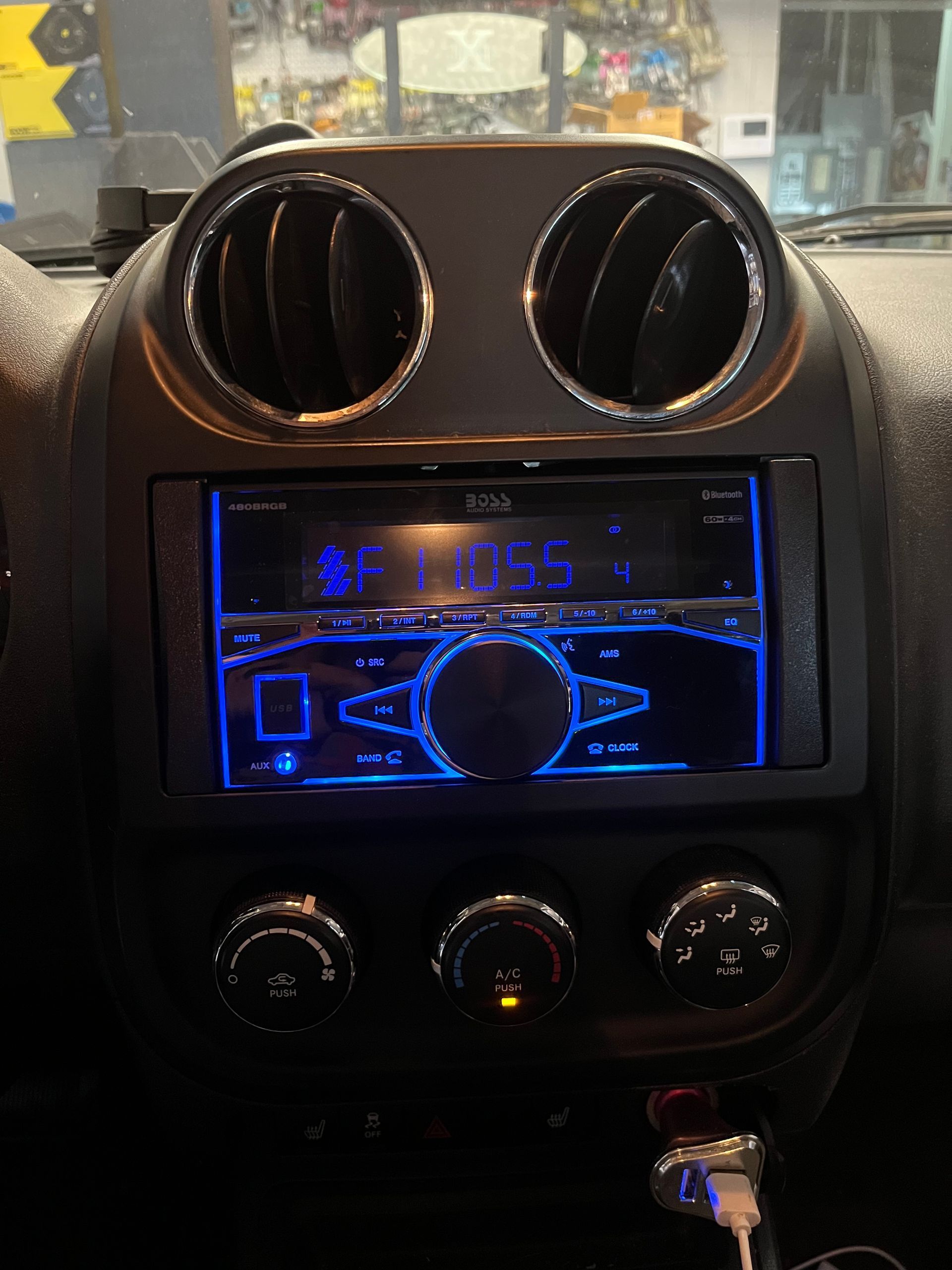 Car dashboard with blue-lit radio display, two circular air vents, and three climate control knobs.