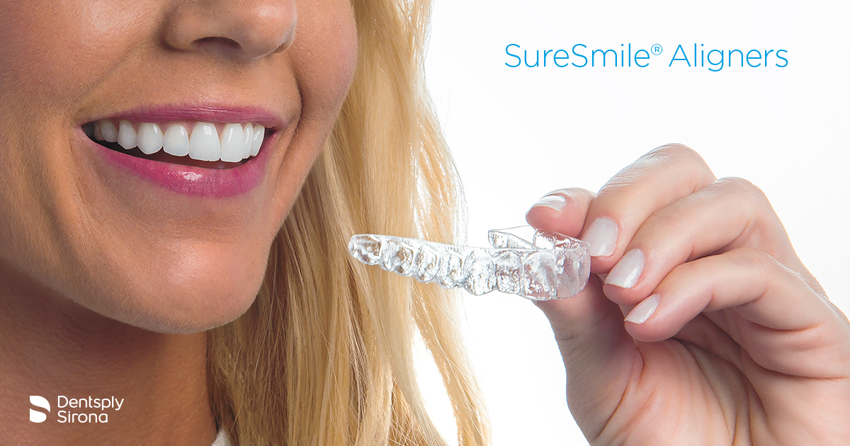 Smiling woman holding a clear SureSmile® aligner, with branding visible.