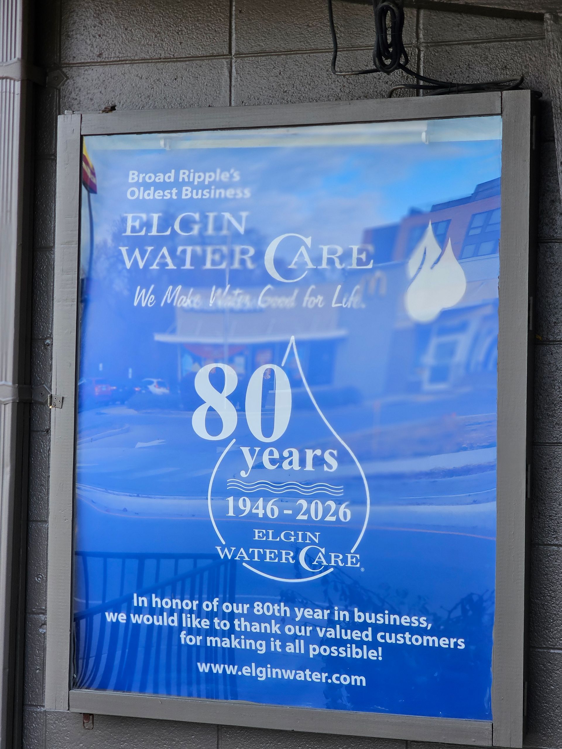 Sign for Elgin Water Care celebrating 80 years. Blue background, with building and water drop graphic.