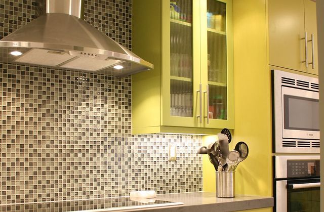 Kitchen with stainless steel hood, mosaic tile backsplash, lime-green cabinets, and built-in oven.