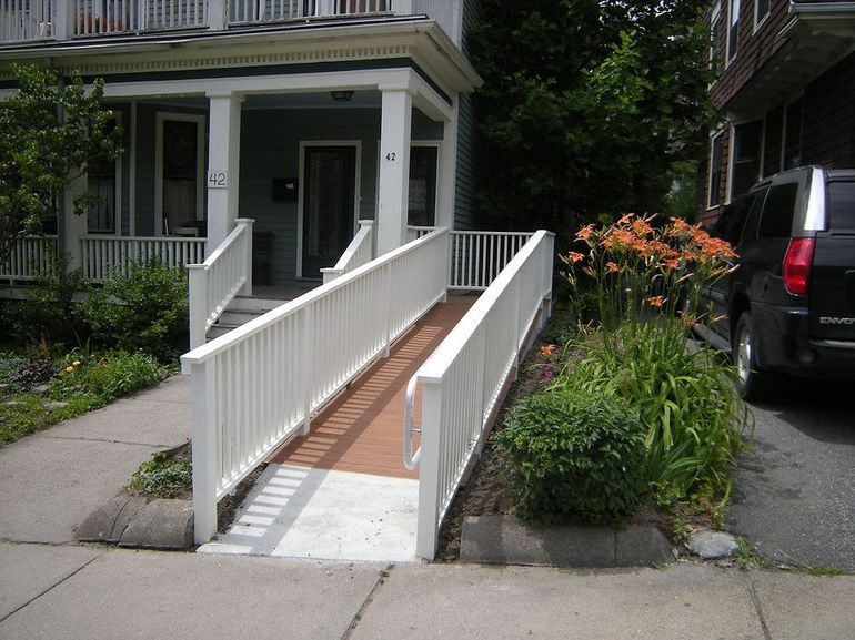 White ramp with railings leading up to the porch of a house, on a sidewalk.