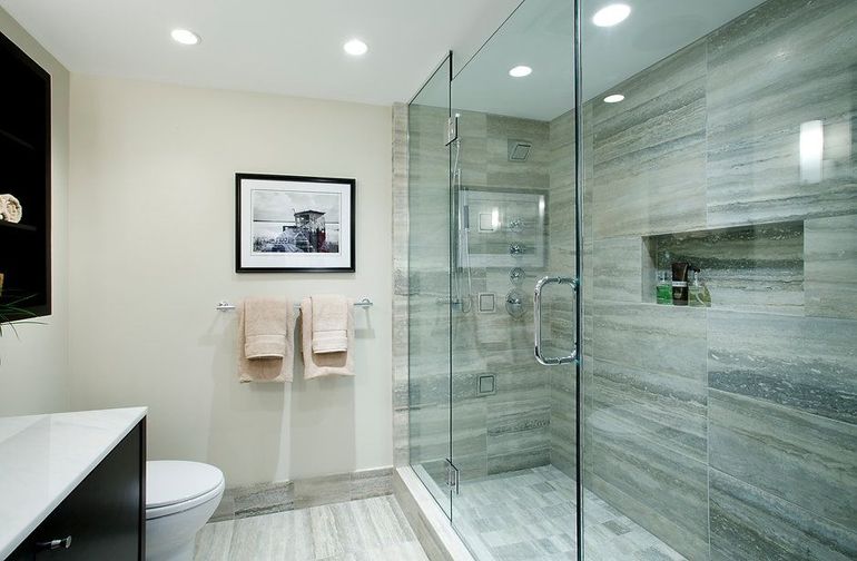 Modern bathroom with glass shower, gray tiled walls, and a toilet.