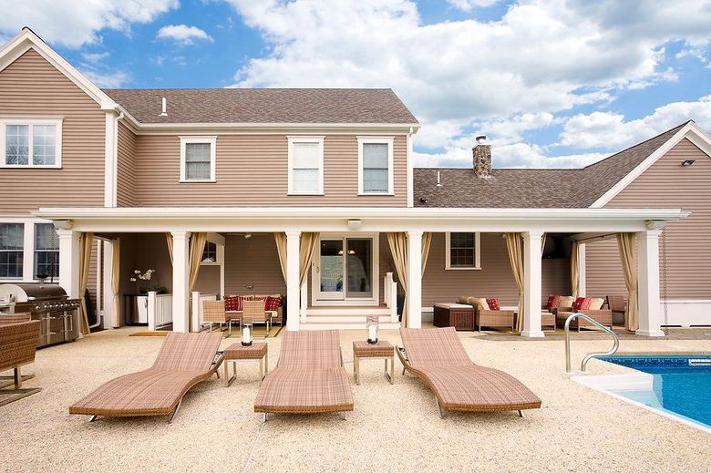 Backyard with pool, lounge chairs, and covered patio with seating, house in background.