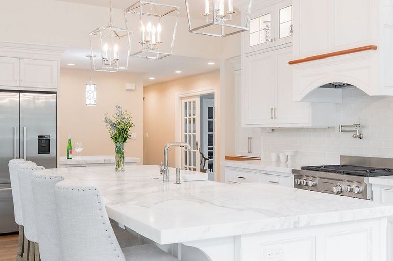 Bright white kitchen with marble island, stainless steel appliances, and modern light fixtures.