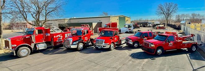 A row of red tow trucks parked outside a building on a sunny day.