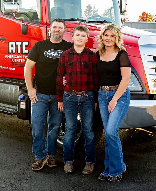 Family posing in front of a red truck; man, teen, and woman smiling.